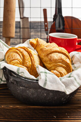 Freshly baked croissant on a napkin with a cup of coffee and a kitchen utensil on the table