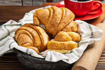 A cup of coffee and a freshly baked croissant on a napkin with a rolling pin on the table
