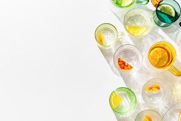 Vivid Glasses with cold detox water as summer still life pattern, shadow and sunlight reflection, closeup glass cups of infused fruit water, slises of lemon, orange, tangerine, healthy summer drink