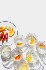 Citrus Infused Water in clear Glasses and plate,  artistic light reflections and shadow in natural sunlight. Summer drink concept, minimal pattern, flavored water with yellow red slices of fruit