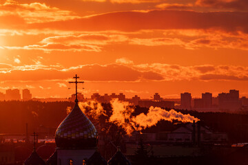Obraz premium Golden sunlight washes over the cityscape as steam rises from building rooftops against a fiery sky