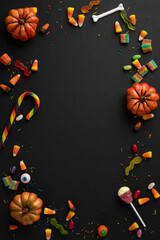 Colorful vertical Halloween candy, decorations, and mini pumpkins forming a border on a dark surface