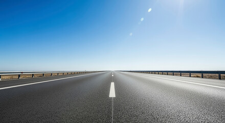 Wide Asphalt Road Stretching Towards the Horizon under a Bright Blue Sky and Warm Sunlight