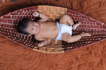 Cute Indian baby lying on a soft textured brown rug, wearing a diaper and traditional black thread bracelets on hands and feet.