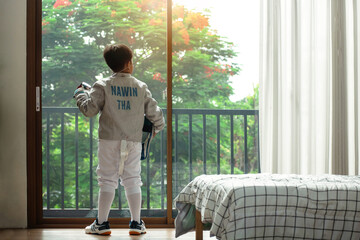 A young fencer stands looking out the window, thinking about today's competition plans.