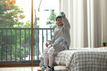 The fencer boy sits on his bed, checking his equipment and thinking about today's competition plan.