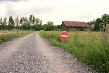 Red and white sign in front of a rural landscape with a house