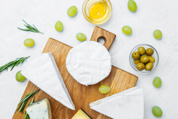 Assorted cheeses with grapes, olives, and honey on a wooden board