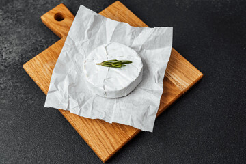 Delicious cheese wheel on wooden cutting board with fresh herbs for flavor