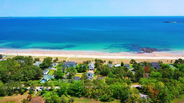 Flying drone captures Saco, Maine beaches alive with people. Crowds line the sand by the Atlantic Ocean, vacation homes in view, waves crash on shore. New England&rsquo;s peak-season coastal beauty.