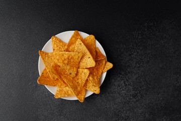 Crispy nacho chips in white bowl with tomato sauce and ingredients on dark and light stone...