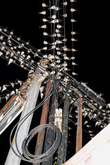 A chaotic web of power lines packed with resting birds under the night sky, forming a surreal pattern of feathers and wires above the quiet street.
