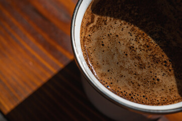  Close-up of fresh coffee with rich crema in a mug on a rustic wooden table. Warm, inviting natural...