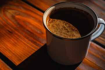  Close-up of fresh coffee with rich crema in a mug on a rustic wooden table. Warm, inviting natural...