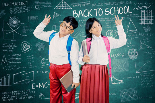 Asian Schoolboy and Schoolgirl Smiling with Three Finger Gesture in Front of Back to School Chalkboard