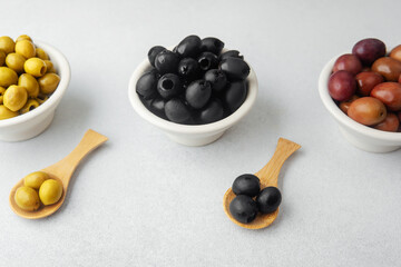 Assortment of green,  black and  kalamata  olives in bowls with wooden spoons