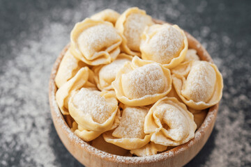 Wooden bowl filled with flour-dusted cappelletti pasta