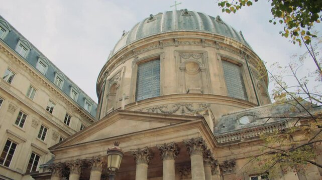 Grand neoclassical church in Paris, with Corinthian columns, ornate detailing, a domed roof, and aged stone facade under partly cloudy sky. Low angle view of Notre-Dame-de-l'Assomption church in Pari