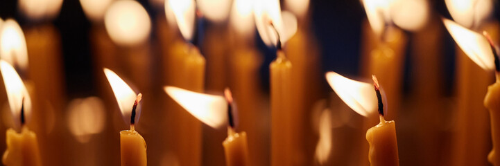Header of multiple burning candles with soft flames in church setting, wax melting and wicks...