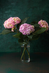 Pink and purple hydrangea bouquet in glass vase on dark green background – ideal for floral wall art, greeting cards, interior decor
