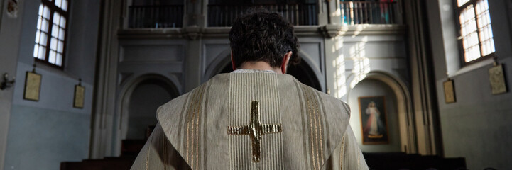 Header of male priest standing with back to camera in church, wearing religious vestment with...