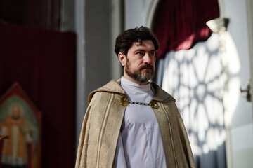 Caucasian middle aged man with beard wearing religious vestments standing in church interior,...