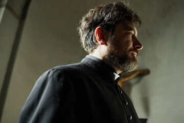 Caucasian middle aged man with beard wearing clerical collar standing in church interior looking to...