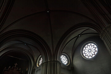 Interior of church showing vaulted ceiling and large circular stained glass windows with intricate patterns, architectural details emphasizing religious setting, no people visible