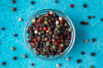 bowl of peppercorns with scattered peppercorns on blue background