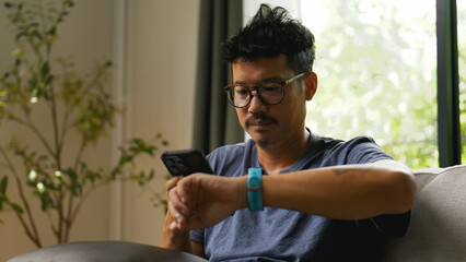 Asian man checking health data on smartwatch at home.