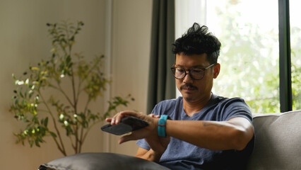 Asian man checking health data on smartwatch at home.