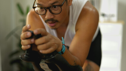 Asian man exercising on a stationary bike at home to stay healthy and fit.