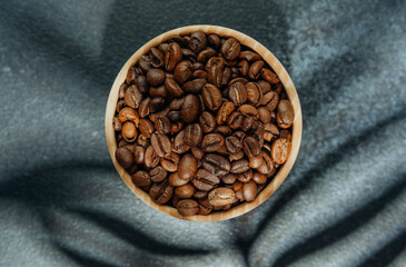 Coffee beans in wooden bowl with leaf shadow on dark background