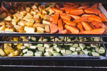 oven with trays of roasted baby potatoes, sweet potatoes and zucchini