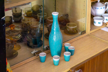 Turquoise decanter with shot glasses in a vintage PRL-style cabinet filled with glassware and...