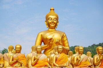 Fototapeta premium The big golden Buddha statue among many small Buddha statues in countryside public temple named MAKHA BUCHA BUDDHIST MEMORIAL PARK, select and soft focus.