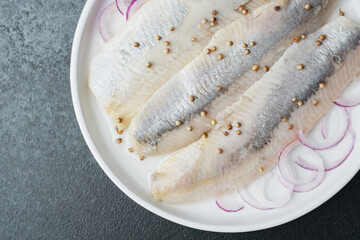 Marinated herring fillets with coriander seeds and onion on white plate over dark background