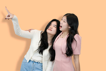 Two Young Asian Women, One Pointing Upward and one looking surprised , Studio Shot