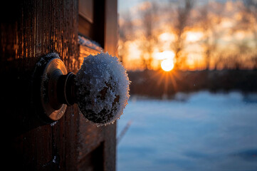 Snowy doorknob glowing against winter sunset