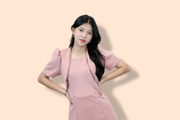 A young Asian woman in a pink dress and bolero smiles confidently at the camera, hand on hip,...