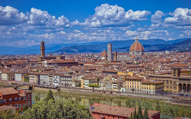 The Arno River winds through Florence, with the grand silhouette of Santa Maria del Fiore Cathedral and the Tower of the Old Palace standing prominently in the city’s historic skyline.