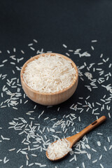 White rice in wooden bowl with scattered grains and wooden spoon