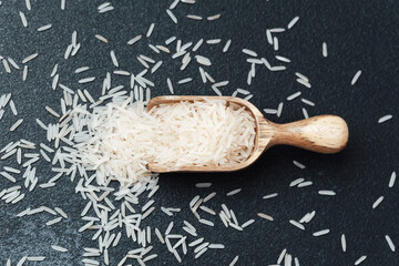 Wooden spoon filled with white rice grains on black surface