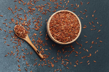 Red rice in wooden bowl with scattered grains and wooden spoon