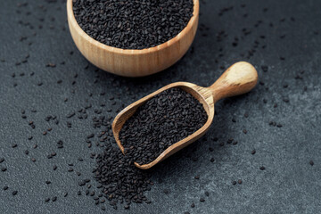 Black sesame seeds in bowl and scoop on dark background