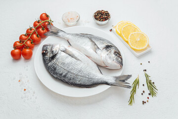 Close up of two dorado fish on white plate with lemon and tomato