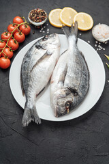 Fresh raw dorado fish on white plate with lemon tomatoes and spices