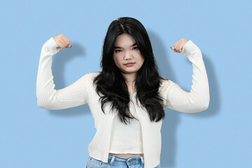 young chinese woman Flexing Biceps Showing Strength and Confidence in blue isolated background