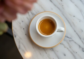 Cafe-style espresso, white cup and saucer, placed on a sophisticated marble counter.



