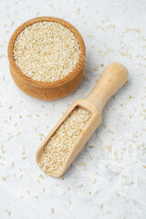 Sesame seeds in a wooden bowl and scoop on a light background
